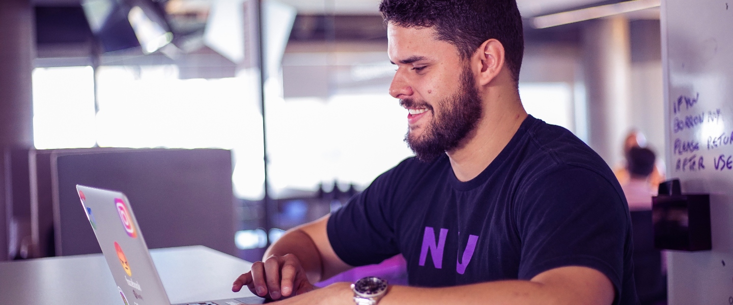 A young bearded man smiles while working with his laptop