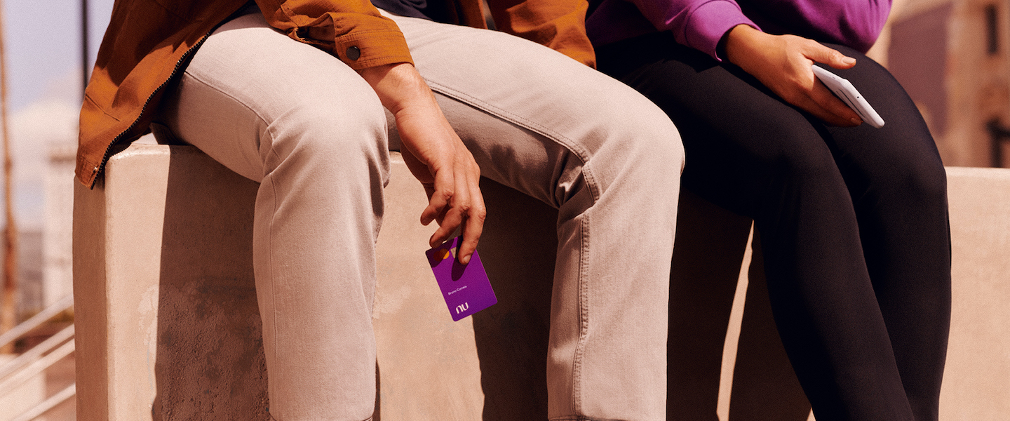 Two people sitting on a wall holding Nubank credit cards